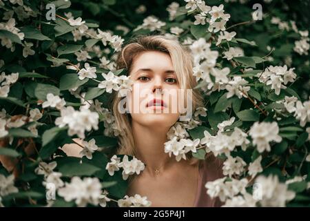 Eine junge schöne Frau in Jasminsträuchern zwischen Blumen. Reine Haut, Duftkonzept, Naturkosmetik Stockfoto