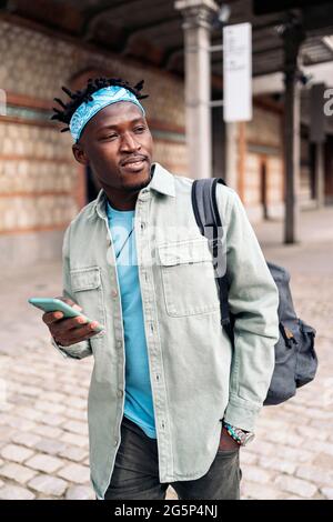Schöner und cooler afrikanischer Mann, der auf der Straße läuft und sein Handy benutzt. Stockfoto