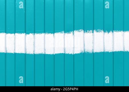 Wandzaun aus Mint-, Türkis- oder Aquamarin-Metall mit vertikalen gewellten Streifen und einem horizontalen Streifen weißer Farbe in der Mitte Stockfoto