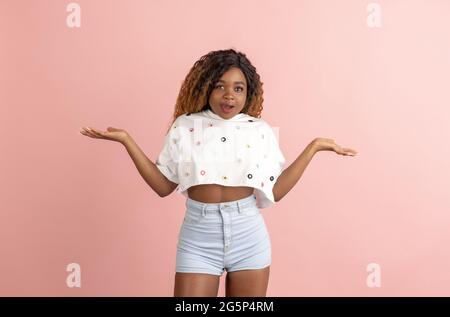 Hübsche afroamerikanische junge Frau in lässiger Kleidung, die auf Pfirsich-Rückengrund posiert und verschiedene Emotionen demonstriert. Stockfoto