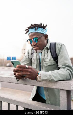 Junger und stilvoller afrikanischer Mann, der auf der Straße steht und sein Handy benutzt. Stockfoto