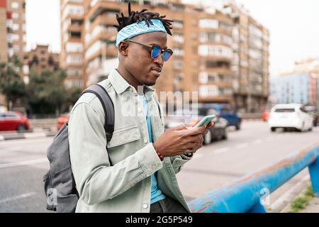 Junger und stilvoller afrikanischer Mann, der auf der Straße steht und sein Handy benutzt. Stockfoto
