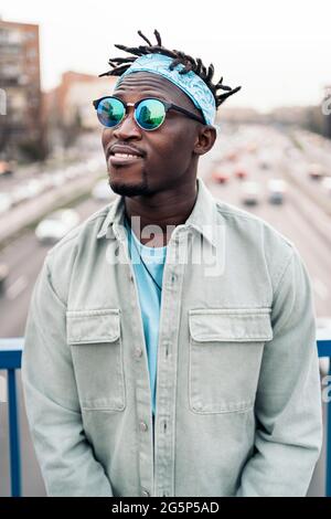 Junger und glücklicher afrikanischer Mann mit Sonnenbrille, der auf der Straße steht und nach vorne schaut. Stockfoto