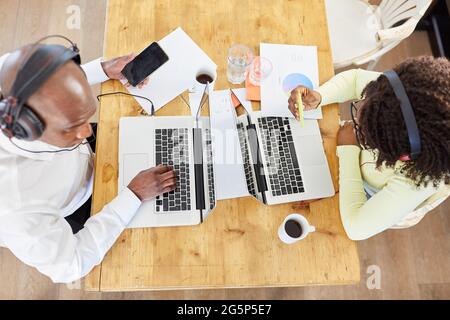 Zwei Geschäftsleute, die im Heimbüro am Tisch im Wohnzimmer an einem Laptop arbeiten Stockfoto