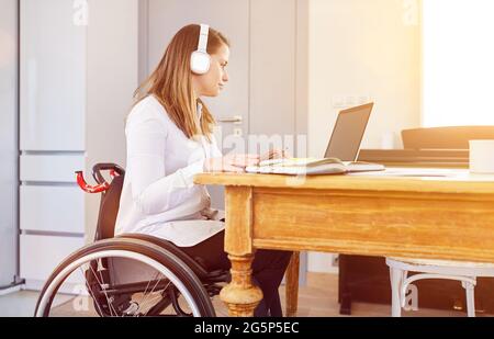 Behinderte Frau im Rollstuhl, die am Heimcomputer im Heimbüro oder Fernunterricht arbeitet Stockfoto