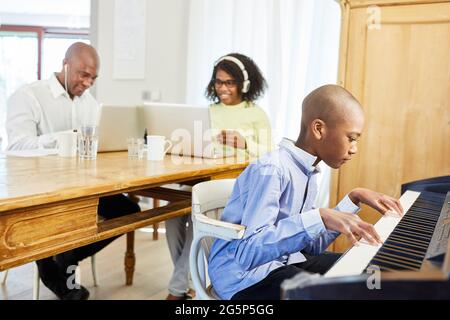 Afroamerikanische Familie, die von zu Hause aus arbeitet, mit Kind, das Klavier spielt Stockfoto