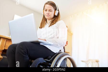 Behinderte Frau im Rollstuhl, die im Heimbüro an einem Laptop arbeitet Stockfoto