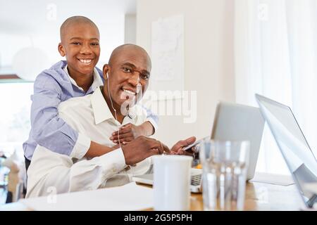 Glückliches Kind als Ablenkung für den Vater während einer Videokonferenz am Computer im Heimbüro Stockfoto