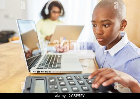 Afrikanischer Junge mit Laptop-Computer, während Heimschooling zu Hause mit Mutter im Hintergrund Stockfoto