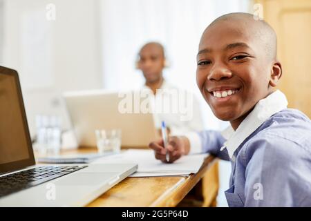 Afrikanischer Junge als glücklicher Schuljunge, der Hausaufgaben im Wohnzimmer macht Stockfoto
