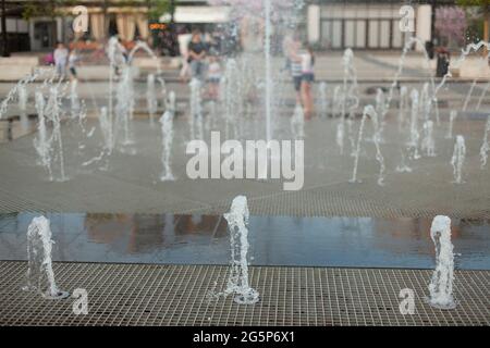 Stadtbrunnen auf dem Platz. Wasser sprudelt aus den Gehwegen. Flugzeugbrunnen in der Stadt. Spritzende Wasserspiele. Stockfoto