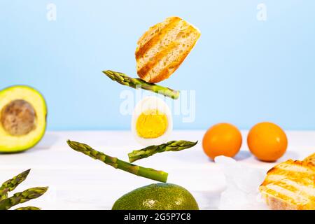 Frisches Brot, Spargel, Avocado und Ei. Zum Frühstück gibt es Inridients. Gleichgewichtsschwimmende Lebensmittel. Balance Levitation Food. Gesunde Vitamin-Ernährung Stockfoto