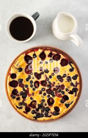 Erdbeer-Blaubeerkuchen auf grauem Hintergrund, eine Tasse mit Kaffee und ein Milchkännchen mit Milch auf dem Tisch, Draufsicht Stockfoto