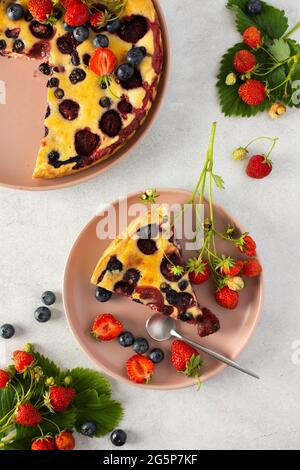 Stück Erdbeer-Blaubeerkuchen mit frischen Beeren auf einem rosa Teller auf grauem Hintergrund, Draufsicht Stockfoto