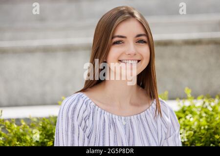 Porträt Einer Lächelnden Jungen Studentin, Die Draußen Auf Dem College-Campus Sitzt Stockfoto