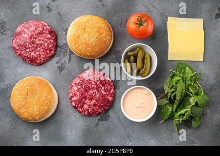 Hausgemachter Hamburger. Hacksteaks, Sesambrötchen mit anderen Zutaten, auf grauem Steingrund, Draufsicht flach liegend Stockfoto