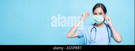 Porträt einer jungen asiatischen schönen Krankenschwester in blauer Uniform und trägt eine chirurgische Maske zum Schutz vor Covid19 oder Coronavirus-Krankheit isoliert in blu Stockfoto