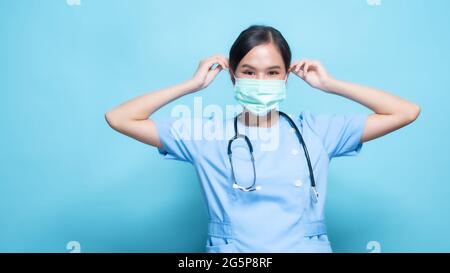Porträt einer jungen asiatischen schönen Krankenschwester in blauer Uniform und trägt eine chirurgische Maske zum Schutz vor Covid19 oder Coronavirus-Krankheit isoliert in blu Stockfoto