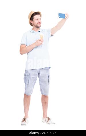 Vertikale volle Länge Seitenansicht Porträt von fröhlich hübsch bärtig kaukasischen Mann trägt Sommer-Outfit hält Eis und Selfie Stockfoto