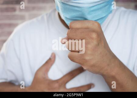 Junger kranker Mann in Gesichtsmaske hustet und niest Stockfoto