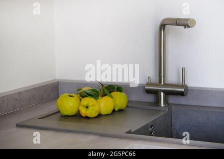 Quittengelb neben dem Waschbecken im Küchenzimmer. Frisches Obst auf der Arbeitsplatte, die in einer modernen Kücheneinrichtung in der Nähe zum Spülen liegt. Gesundes Lebensmittelkonzept. Stockfoto