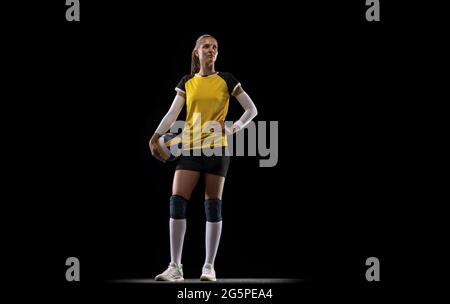 Junge Volleyballspielerin isoliert auf schwarzem Studiohintergrund. Frau in Sportausrüstung und Schuhen oder Turnschuhen, die trainieren und üben. Stockfoto