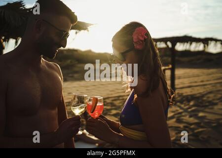 Ein romantisches Paar, das bei Sonnenuntergang am Strand toaste. Reise- und Alkoholkonzept Stockfoto