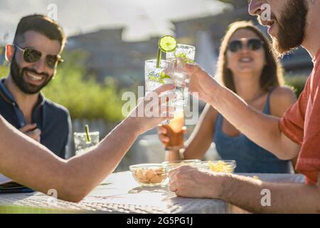 Wiedervereinigung der besten Freunde beim Toasten mit Longdrinks im Pub im Freien. Happy Hour mit tropischen Cocktails bei Sonnenuntergang im Sommer. Stockfoto