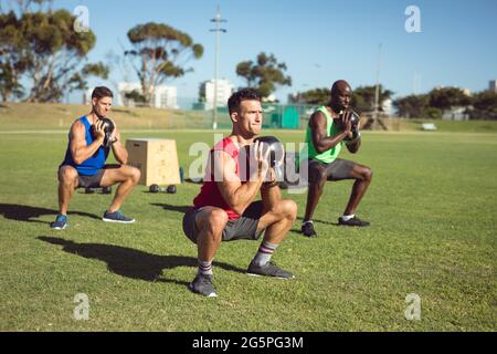 Diverse Gruppe von muskulösen Männern trainieren mit Wasserkocher Glocken im Freien Stockfoto