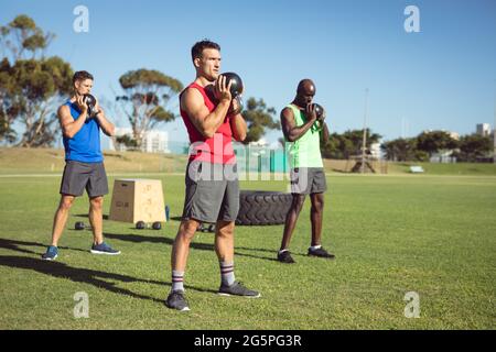 Diverse Gruppe von muskulösen Männern trainieren mit Wasserkocher Glocken im Freien Stockfoto