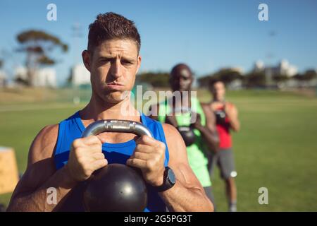 Diverse Gruppe von muskulösen Männern trainieren mit Wasserkocher Glocken im Freien Stockfoto