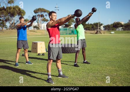 Diverse Gruppe von muskulösen Männern trainieren mit Wasserkocher Glocken im Freien Stockfoto