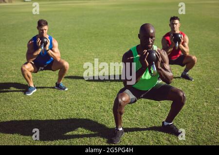 Diverse Gruppe von muskulösen Männern trainieren mit Wasserkocher Glocken im Freien Stockfoto