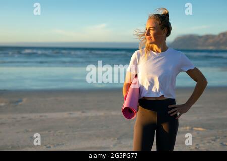 Porträt einer kaukasischen Frau, die Yoga praktiziert, am Strand steht und Pause macht Stockfoto