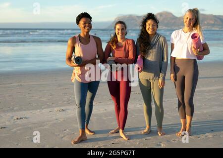 Eine Gruppe verschiedener Freundinnen, die Yoga praktizieren, am Strand stehen und Pause machen Stockfoto