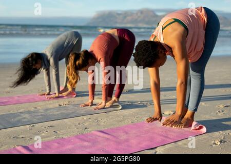 Eine Gruppe verschiedener Freundinnen, die Yoga praktizieren und am Strand meditieren Stockfoto