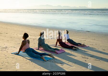 Eine Gruppe verschiedener Freundinnen, die Yoga praktizieren, am Strand liegen und starren Stockfoto