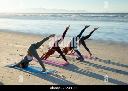 Eine Gruppe verschiedener Freundinnen, die Yoga praktizieren und sich am Strand strecken Stockfoto