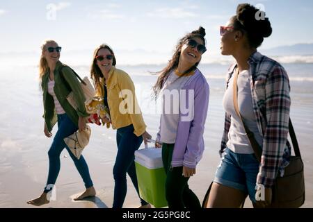 Fröhliche Gruppe verschiedener Freundinnen, die Spaß haben, am Strand entlang spazieren und lachen Stockfoto