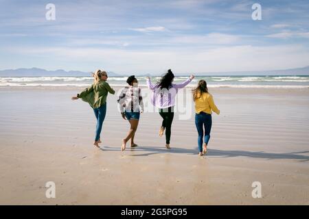 Glückliche Gruppe von verschiedenen Freundinnen, die Spaß haben, am Strand entlang zu laufen Stockfoto