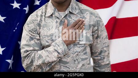 Zusammensetzung des Mittelteils des männlichen Soldaten mit Hand auf Herz, gegen die amerikanische Flagge Stockfoto