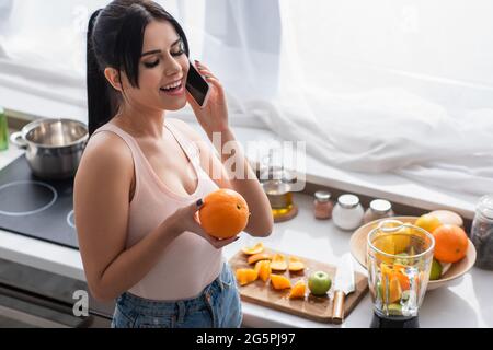 Glückliche Frau, die auf dem Smartphone spricht und orange hält Stockfoto