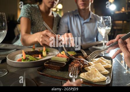 Eine Gruppe von multirassischen Freunden, die Spaß beim Essen im asiatischen Restaurant haben, aber Gabeln benutzen. Europäisches Restaurant mit asiatischer Küche. Stockfoto