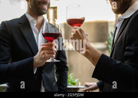 Zwei Geschäftsleute in Anzug stehen im Hotelzimmer und unterhalten sich mit Weinläsern und trinken zusammen. Freistellungsaufnahme Stockfoto
