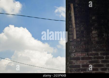 Der Himmel ist hellblau mit einer Hauswand aus massivem rotem Backstein. An der Wand ist noch ein Stück Holz angebracht, das von der Konstruktion des übrig geblieben ist Stockfoto