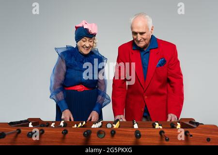 Positive ältere Paar in stilvoller Kleidung spielen Tischfußball auf grau Stockfoto