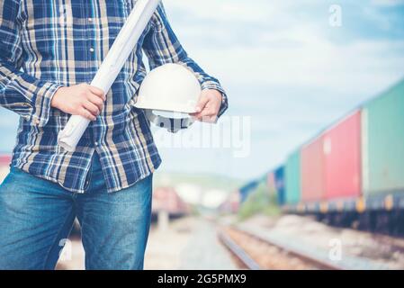 Bauingenieurteam mit Bauplan für das Projekt vor Ort, das in der Produktionsanlage für Eisenbahngleise arbeitet. Konzept Der Industrietechnik. Stockfoto