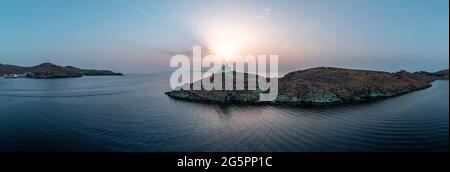 Kea Tzia Insel. Griechenland, Kykladen. Leuchtturm auf einem felsigen Kap bei Sonnenuntergang, Drohne, Luftpanorama. Korissia Hafen und gewelltes Meerwasser Hintergrund. Stockfoto