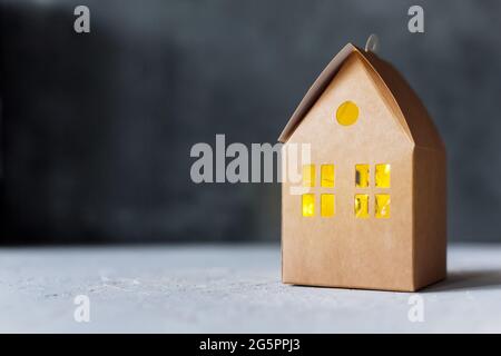 Bastelkarton Box House mit leuchtendem Fenster, kreative Geschenkverpackung auf grauem Hintergrund Stockfoto