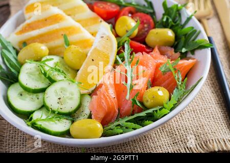 Ketogen, Keto-Diät. Gesalzener Lachs, gegrillter Halloumi-Käse, Kirschtomaten und Gurkensalat mit Oliven in einer weißen Schüssel. Gesunde Ernährung. Stockfoto